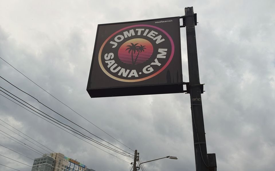 Round Jomtien Sauna & Gym sign on a tall pole against a cloudy sky