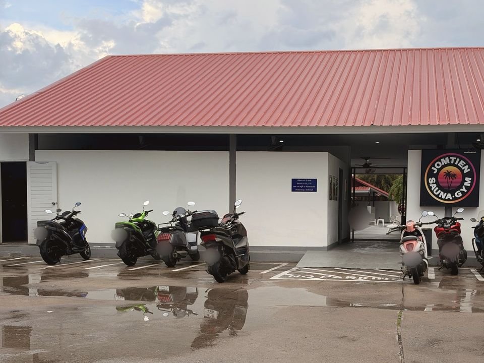 Front of Jomtien Sauna & Gym: red roof, the round logo sign by the entrance and parked motorbikes