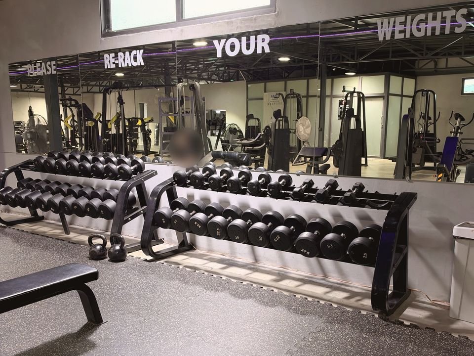 Стойки с гантелями у зеркальной стены с надписью «Please re-rack your weights»
